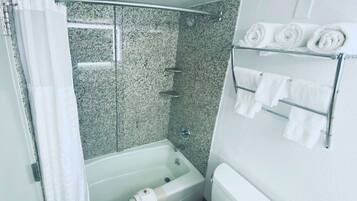 A bathroom with a bathtub, shower, and toilet. There are towels on a rack.