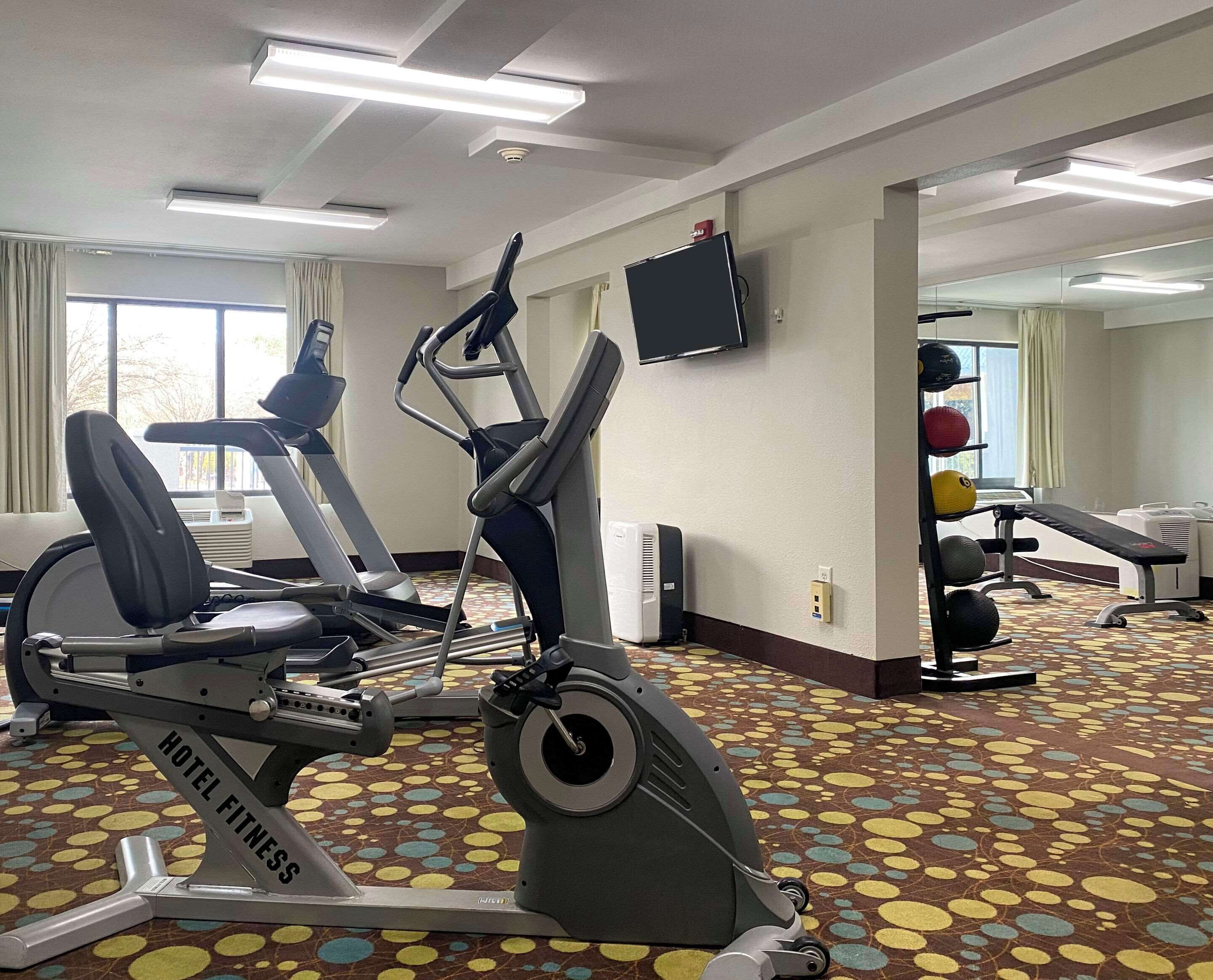 Un gimnasio de hotel con cintas de correr, una bicicleta estática y un banco para pesas.