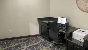 Habitación de hotel con escritorio, computadora, impresora y alfombra estampada.