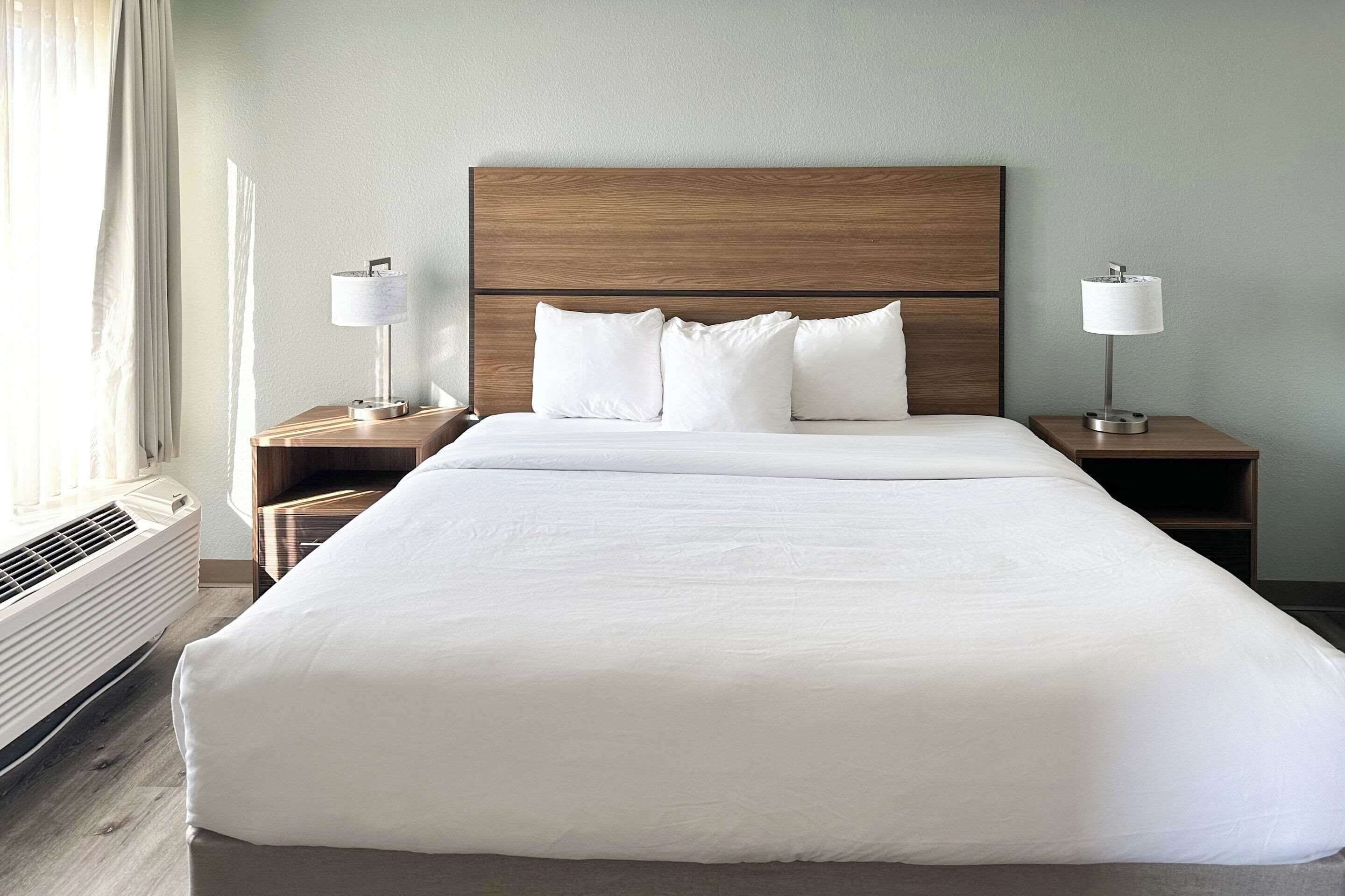 Una cama bien tendida con sábanas blancas, un cabecero de madera y dos mesitas de noche con lámparas.