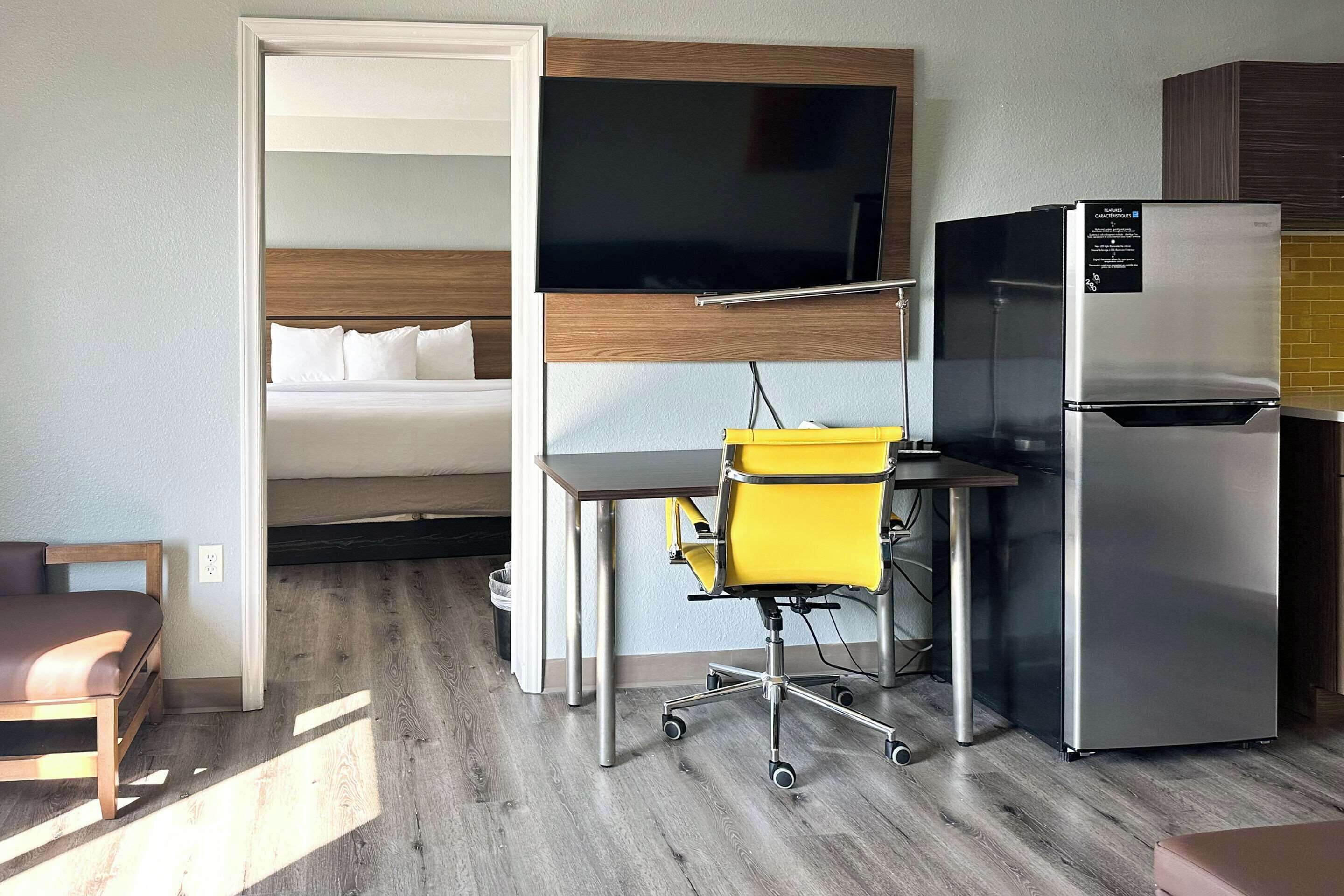 Pieni hotellihuone, jossa on sänky, työpöytä tuolilla, televisio ja jääkaappi.