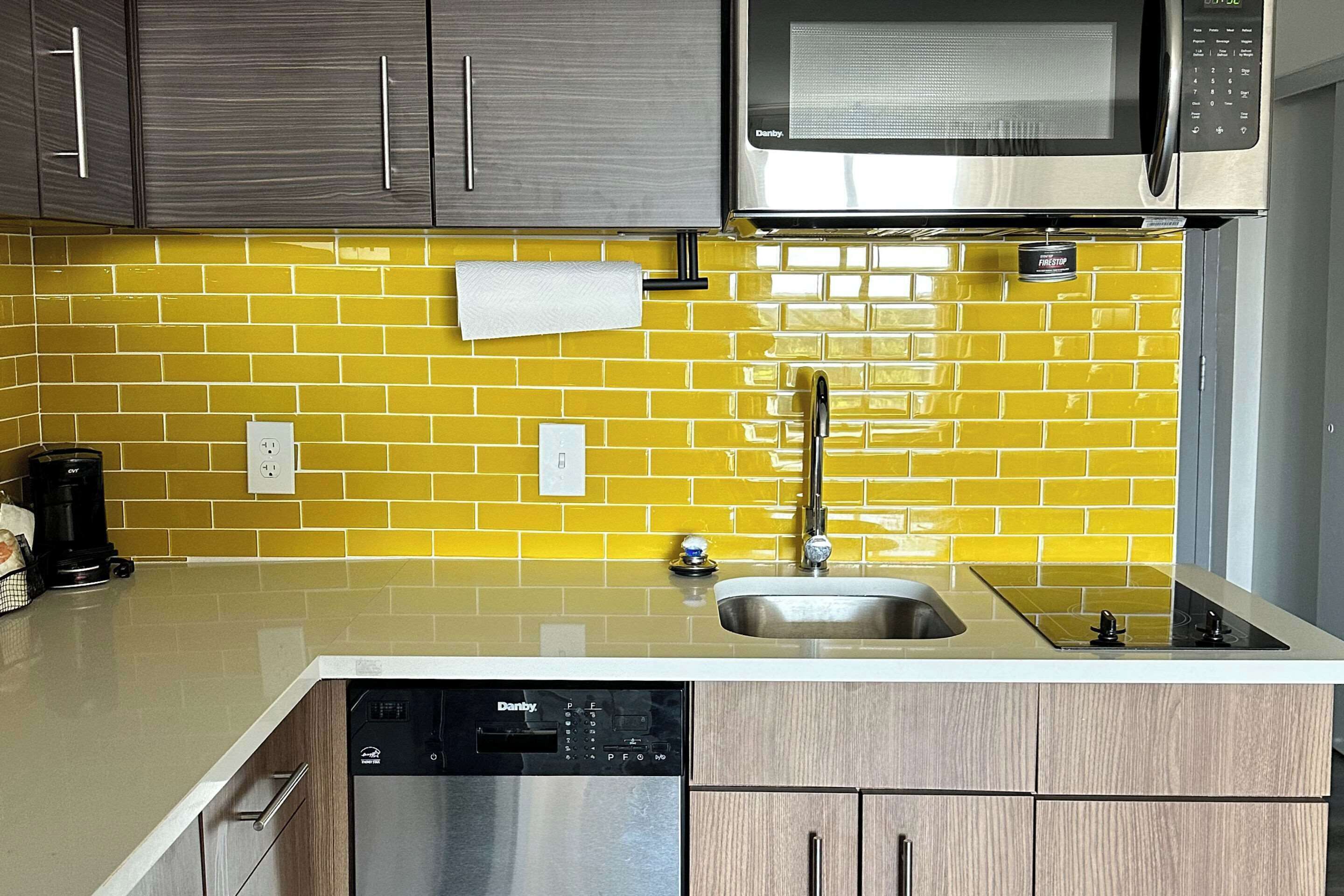 A kitchen with a yellow-tiled backsplash, a stainless steel microwave, a dishwasher, and a sink.