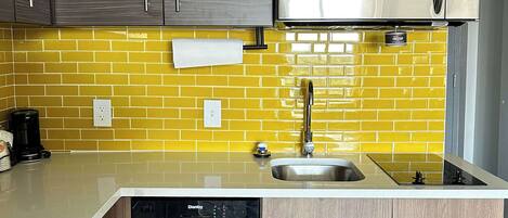 A kitchen with a yellow-tiled backsplash, a stainless steel microwave, a dishwasher, and a sink.