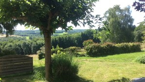 Un espace extérieur verdoyant, avec un banc en bois, un arbre et une vue sur un paysage vallonné.