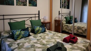 Habitación de hotel con una cama, almohadas verdes, una mesita de noche, un espejo y obras de arte con motivos tropicales en la pared.
