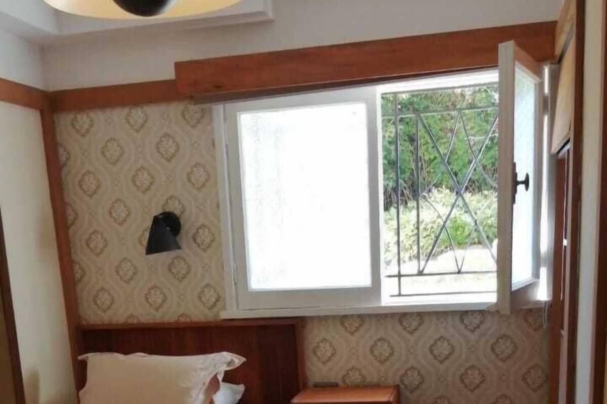Een kleine kamer met een enkel bed, een raam, een nachtkastje en behang met een patroon.