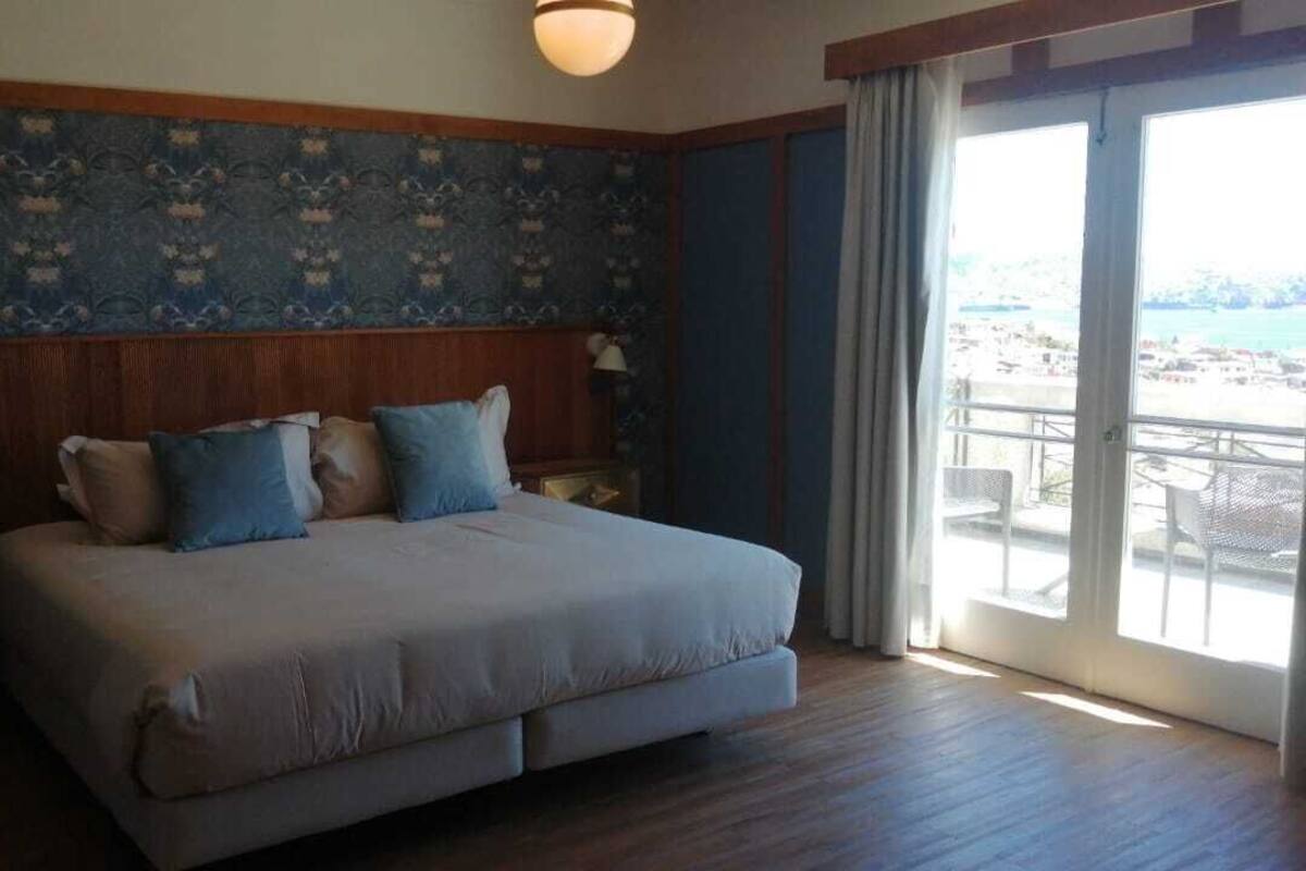 Een hotelkamer met een groot bed, een houten hoofdbord en uitzicht op het strand vanaf het balkon.