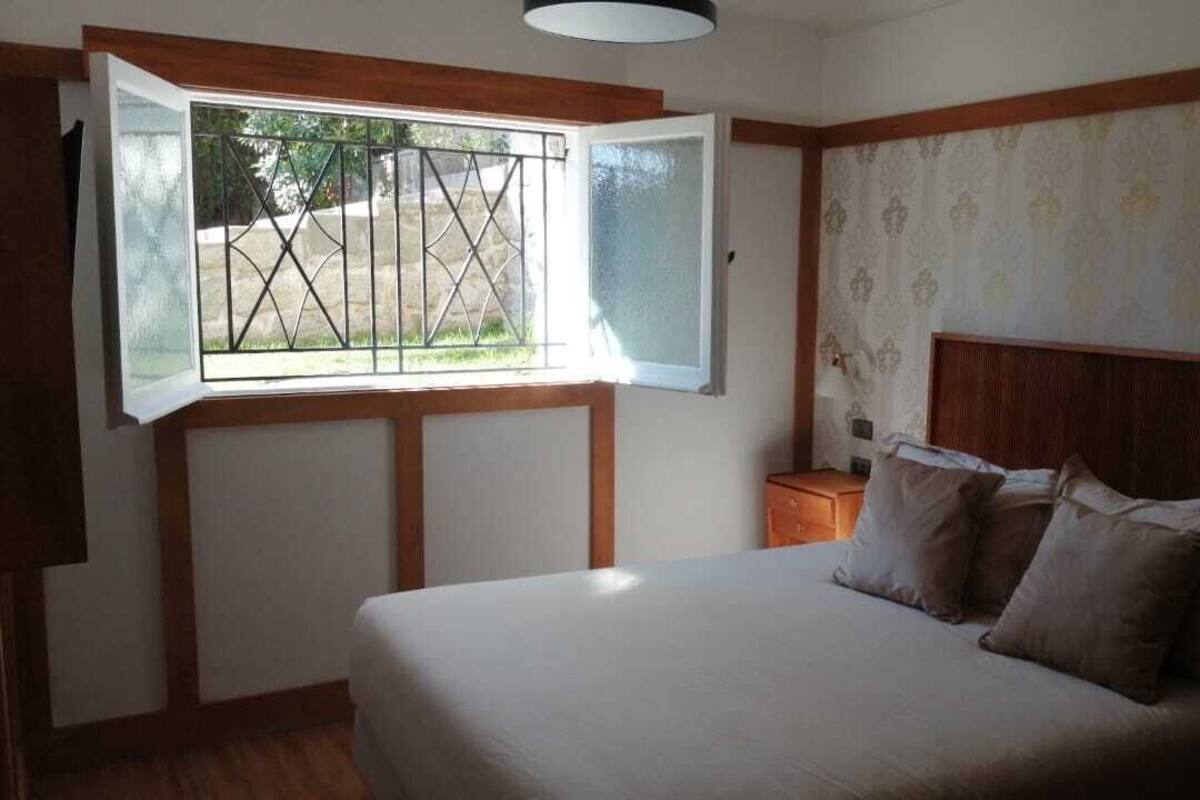 Een slaapkamer met een bed, een nachtkastje, een raam met een metalen traliewerk en behang met een patroon op de muur.