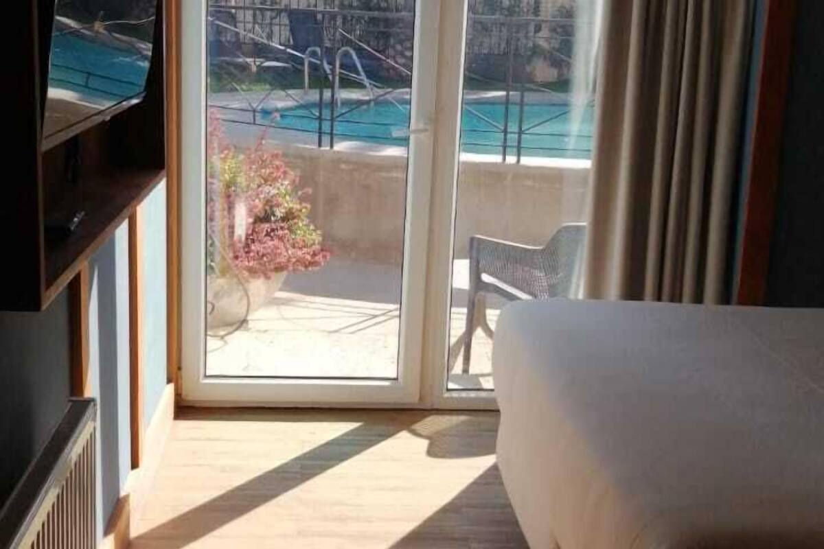 Een hotelkamer met een bed, een televisie en uitzicht op een zwembad en terras.