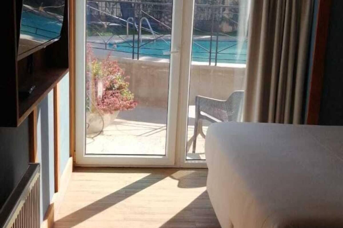 Een hotelkamer met een bed, een televisie, een glazen schuifdeur naar een zwembad en een stoel.
