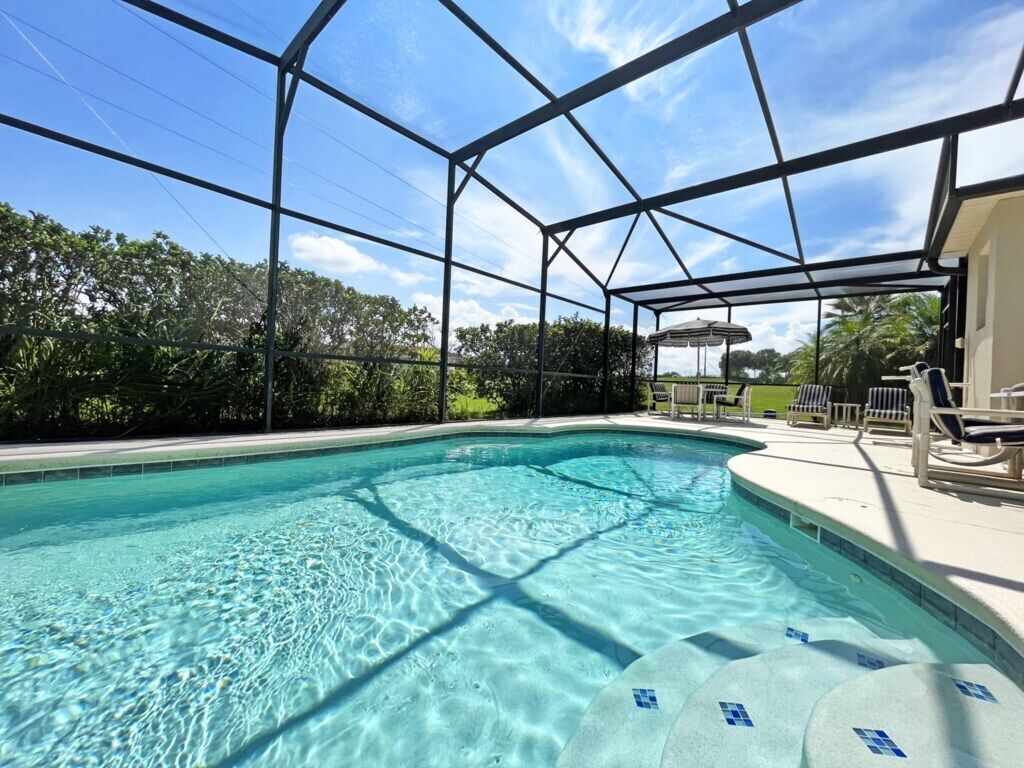 Piscina transparente com estrutura de cobertura metálica, rodeada por cadeiras de descanso e uma área coberta.