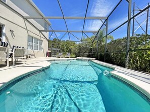 Une piscine à l’eau d’un bleu limpide, entourée d’une zone abritée avec des chaises, et un bâtiment visible au fond.