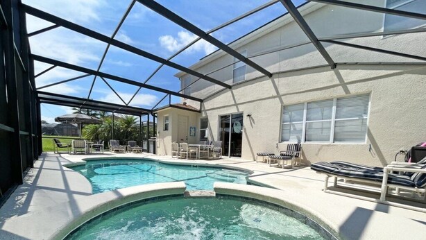 A pool area with a glass-enclosed structure, lounge chairs, and a small building with a door. - Spacious pool home with games room and hot tub (heating included) (Davenport)
