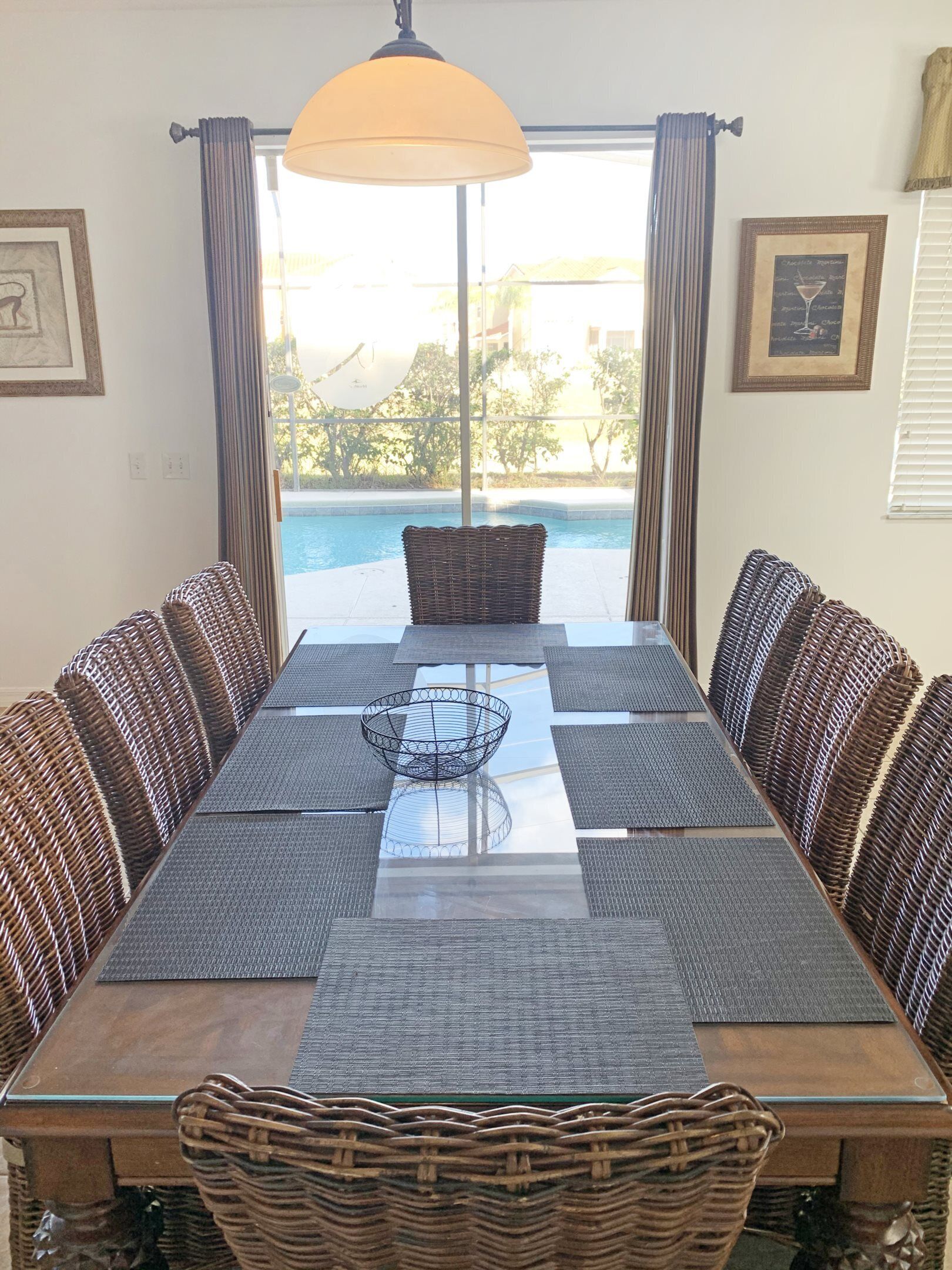A dining area with a long table, wicker chairs, and a view of a swimming pool.