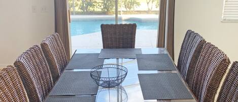 A dining area with a long table, wicker chairs, and a view of a swimming pool.