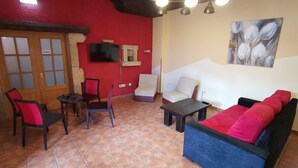 Un salón con una pared roja, un televisor sobre la chimenea, un sofá, un sillón y una mesita.