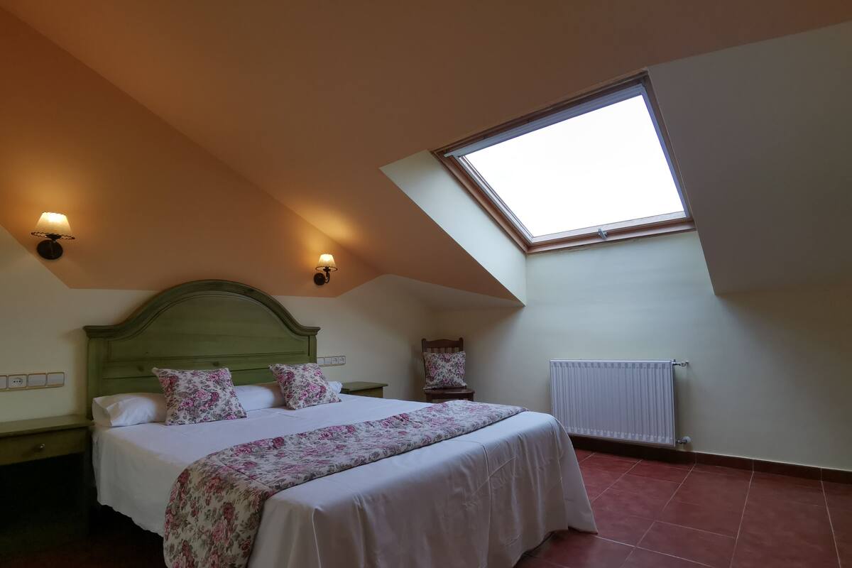 A bedroom with a sloped ceiling, a skylight, a bed with floral bedding, and a radiator.