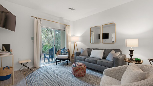 A modern living room with a grey sofa, a round ottoman, and a blue and white striped rug. - 🐟1st Floor with Bikes-Coach's Sand Dollar (Santa Rosa Beach)