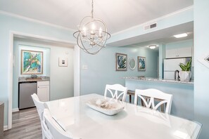 A modern kitchen with white cabinets, a stainless steel refrigerator, and a dining area with a white table and chairs.