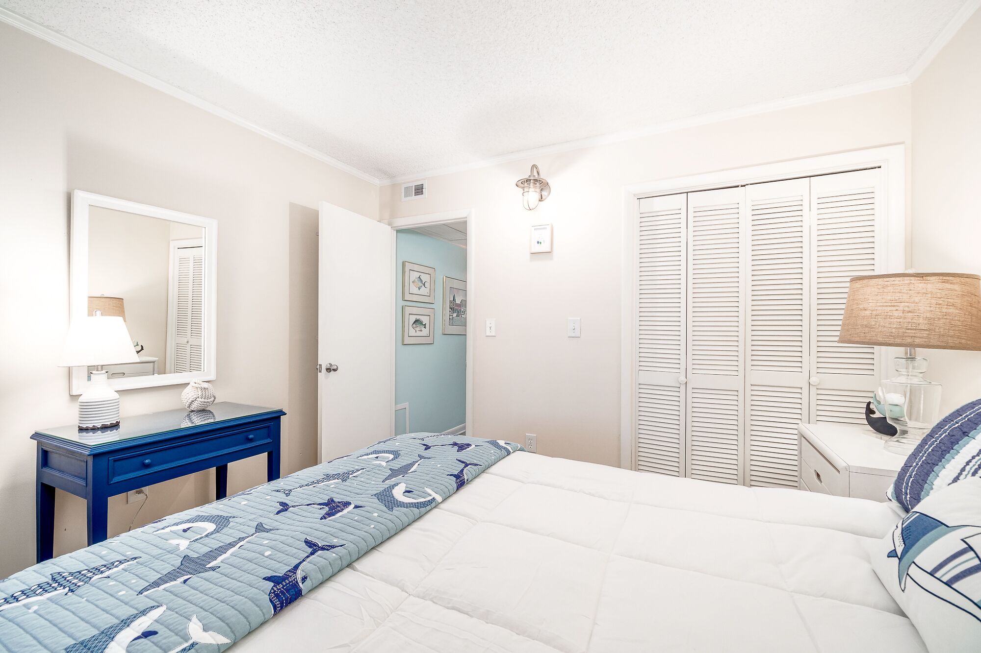Quarto com cama, cómoda, espelho, guarda-roupa e porta que dá para outro espaço.