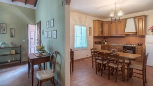 A spacious kitchen with wooden cabinets, a dining table with chairs, and a chandelier. - LA ROSA CANINA     . (Castiglione del Lago)