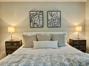 A neatly made bed with a fluffy white blanket, two bedside tables with lamps, and two framed wall art pieces above the bed.