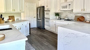 A modern kitchen with white cabinetry, a stainless steel refrigerator, a microwave, and a gas stove. - Palm Springs Private Home • Gated Cul‑de‑Sac • Pool, Spa & Backyard (Palm Springs)