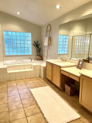 A modern bathroom with a large bathtub, two sinks, a mirror, and a potted plant.