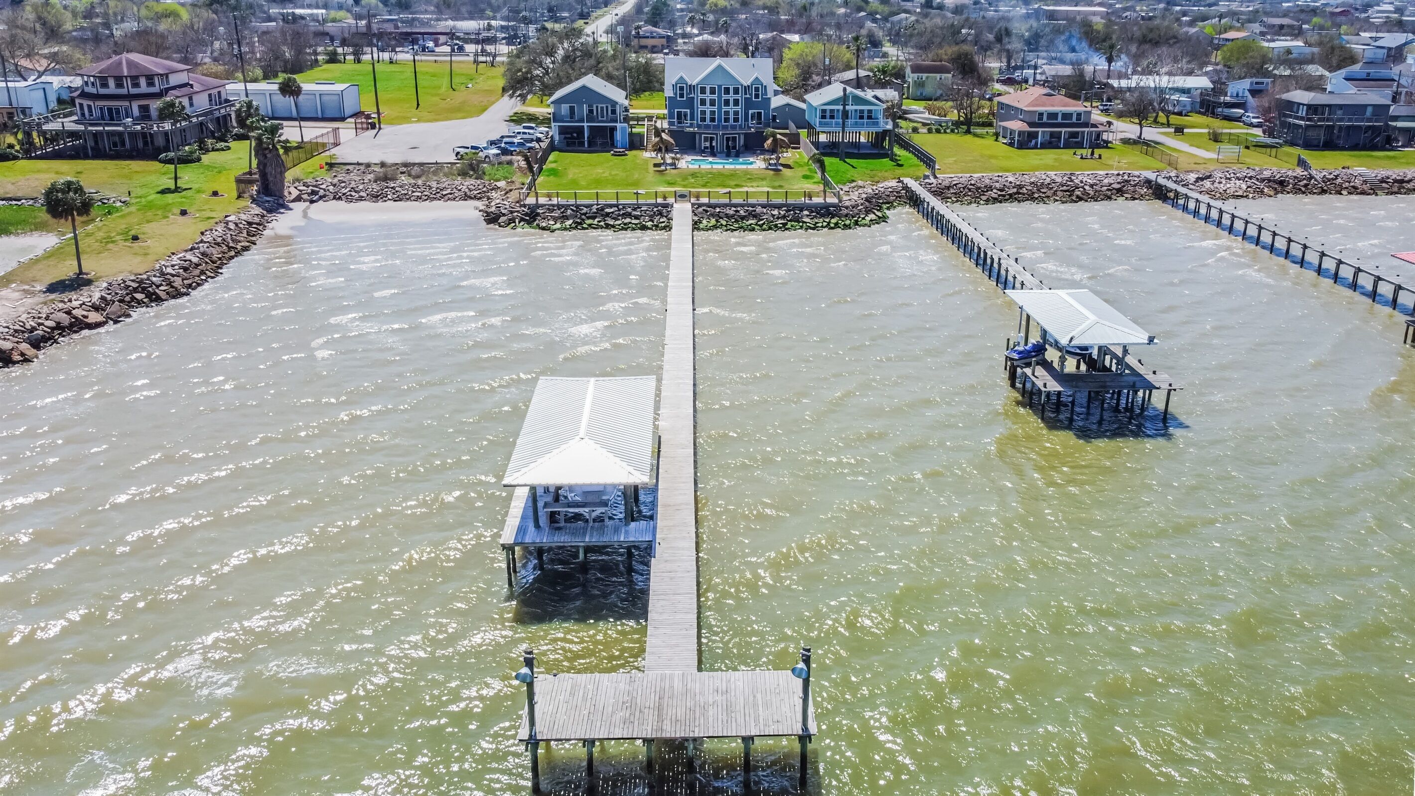 Een pand aan het water met een lange houten steiger die uitkomt op een centrale pier, omringd door woongebouwen en een zwembad.