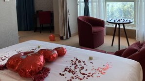 A hotel room with a large bed, a red armchair, a small table, and a view of the outdoors through a window. - Hotel El Amine (Boumerdès)