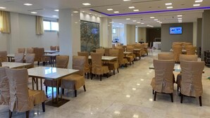 A spacious hotel dining area with multiple tables and chairs, a large mural on the wall, and a television screen on the wall. - Hotel El Amine (Boumerdès)