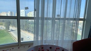 A room with a large window, a round table with rose petals, and a red chair. - Hotel El Amine (Boumerdès)
