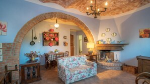 A cozy living room with a floral sofa, a fireplace, and a dining area with a table and chairs. - IL GIAGGIOLO       . (Castiglione del Lago)