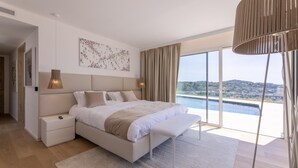 A modern bedroom with a large bed, a nightstand, a bedside lamp, and a view of a body of water through large windows. - Luxury Villa for Rent Mougins (Mougins)
