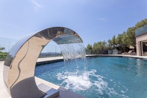 Ein moderner Pool mit einer metallischen Bogenstruktur und herabfließendem Wasser.