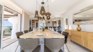 A modern dining area with a large wooden table, six chairs, and hanging pendant lights. - Luxury Villa for Rent Mougins (Mougins)