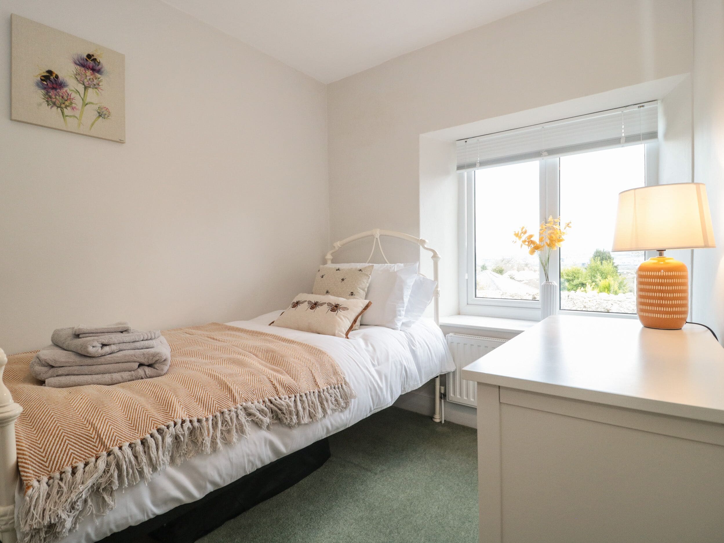 A neatly arranged bedroom with a bed, bedside table, lamp, and a window with a view.