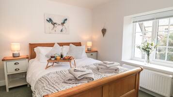 A neatly made bed with a tray of breakfast items, two bedside lamps, a wall art piece, and a window with a view of buildings.
