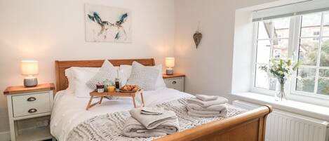 A neatly made bed with a tray of breakfast items, two bedside lamps, a wall art piece, and a window with a view of buildings.