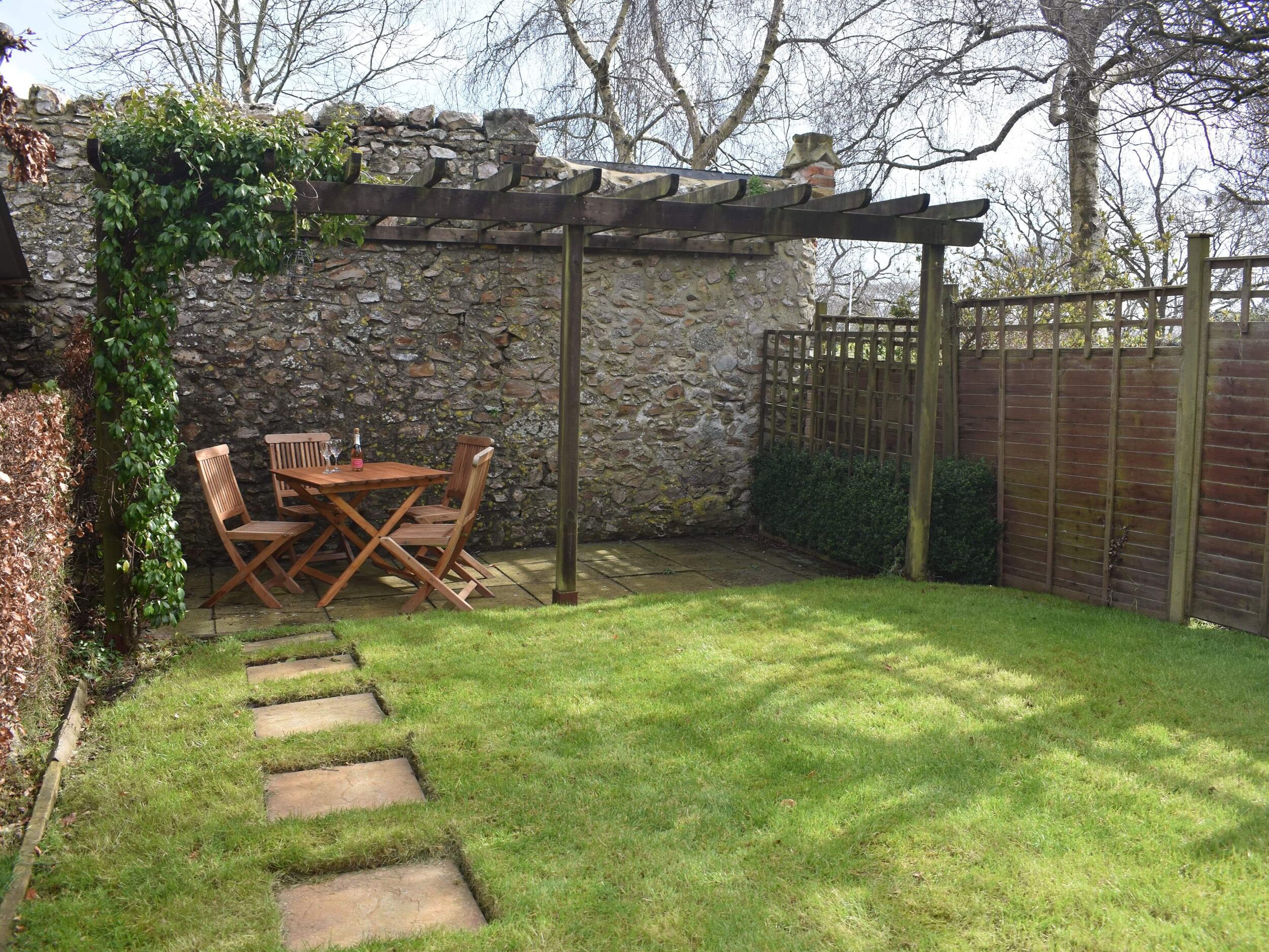 A stone wall with a wooden pergola and a table with chairs.
