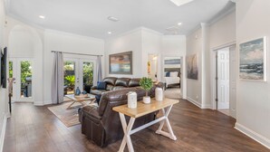 A spacious living room with a brown leather sofa, a wooden coffee table, and a large painting on the wall. - Spacious Ocean Retreat~Minutes to the Beach, BBQ, Pool, Beach Gear, and More! (Destin)