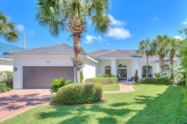 A two-story house with a garage, palm trees, and a well-maintained lawn. - Spacious Ocean Retreat~Minutes to the Beach, BBQ, Pool, Beach Gear, and More! (Destin)