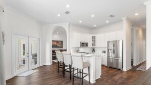 A modern kitchen with white cabinetry, stainless steel appliances, and a central island with bar stools. - Spacious Ocean Retreat~Minutes to the Beach, BBQ, Pool, Beach Gear, and More! (Destin)