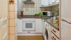 Een compacte keuken met witte kastjes, een fornuis, een magnetron en een wasmachine.