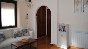 Een woonkamer met een bank, een bijzettafeltje, een boekenkast en een houten deur.