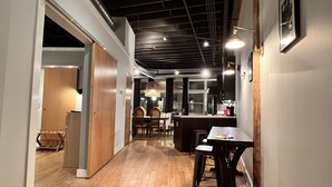 A modern kitchen with wooden flooring, a dining area with a table and chairs, and a bar area with stools. - Ambrose Lofts - 1 bedroom overlooking 4th Ave Downtown (Nashville)