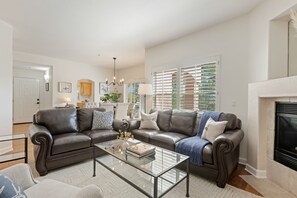 A living room with a fireplace, leather sofas, a glass coffee table, and a view of the outdoors through large windows.
