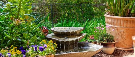 A tiered stone fountain surrounded by potted plants and flowers in a garden setting.