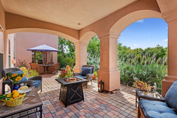 An outdoor patio with a fire pit, wicker furniture, and a view of a garden.