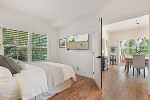 A bedroom with a bed, a painting, and a TV on the wall.